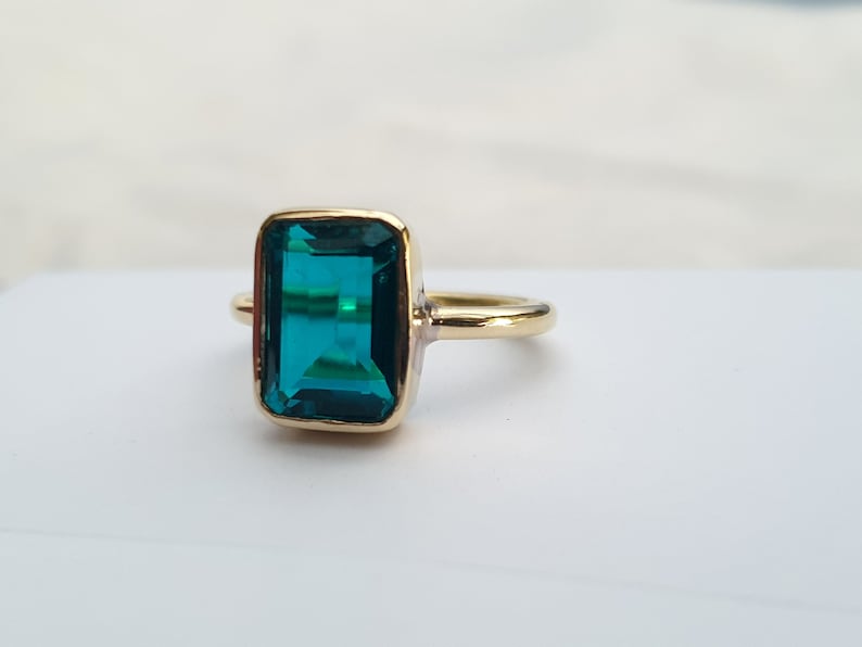 May include: A gold ring with a large, emerald green gemstone. The gemstone is cut in a rectangular shape.