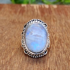 May include: A silver ring with a large oval moonstone set in a detailed silver bezel. The ring has a braided design around the stone.