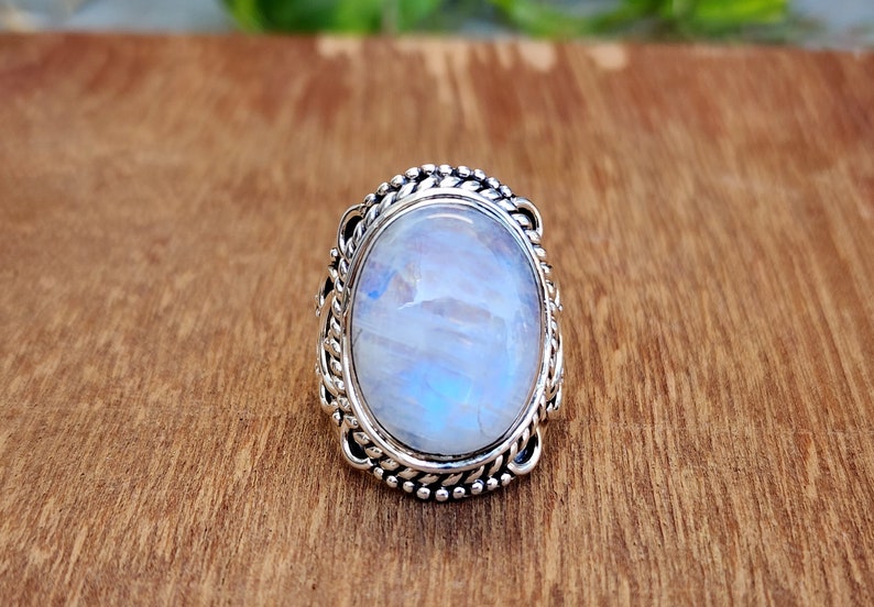 May include: A silver ring with a large oval moonstone set in a detailed silver bezel. The ring has a braided design around the stone.