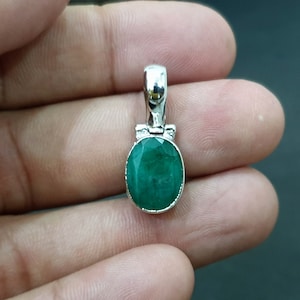 Puede incluir: Un colgante de plata con una esmeralda ovalada verde.