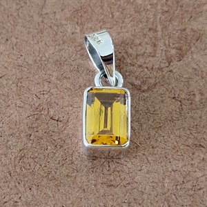 May include: A silver pendant with a rectangular, yellow gemstone.