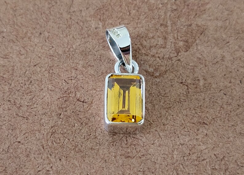 May include: A silver pendant with a rectangular, yellow gemstone.