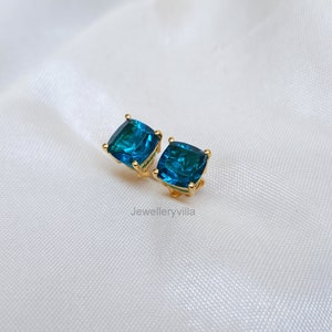 Puede incluir: Un par de pendientes de bot&oacute;n de oro con piedras azules de forma cuadrada.