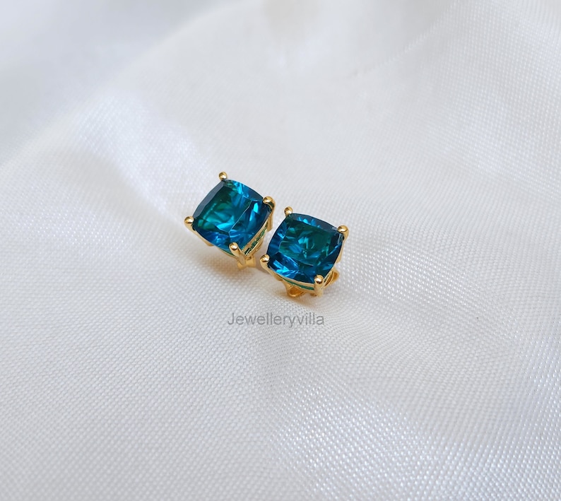 Puede incluir: Un par de pendientes de bot&oacute;n de oro con piedras azules de forma cuadrada.