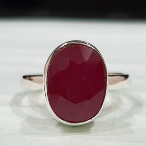 May include: A silver ring with a large, oval-shaped, deep red gemstone.