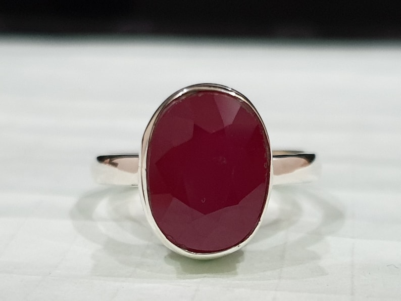 May include: A silver ring with a large, oval-shaped, deep red gemstone.