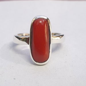 May include: A silver ring with a red oval-shaped gemstone.