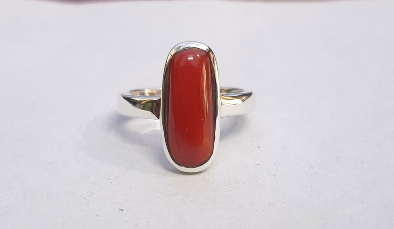 May include: A silver ring with a red oval-shaped gemstone.