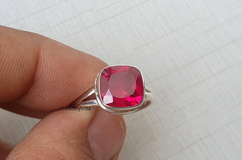 May include: A silver ring featuring a large, square-shaped, red gemstone.