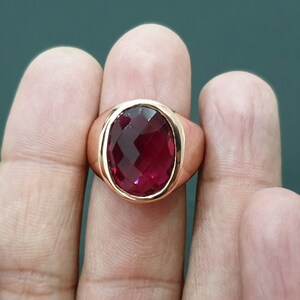May include: A gold ring with a large, oval-shaped, faceted, dark red gemstone.
