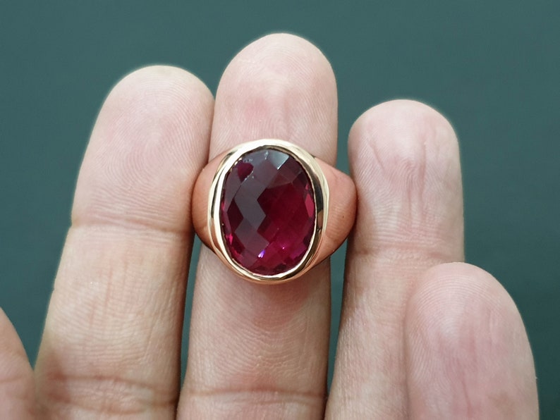 May include: A gold ring with a large, oval-shaped, faceted, dark red gemstone.