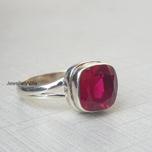 May include: A silver ring featuring a large, square-shaped, deep red gemstone.