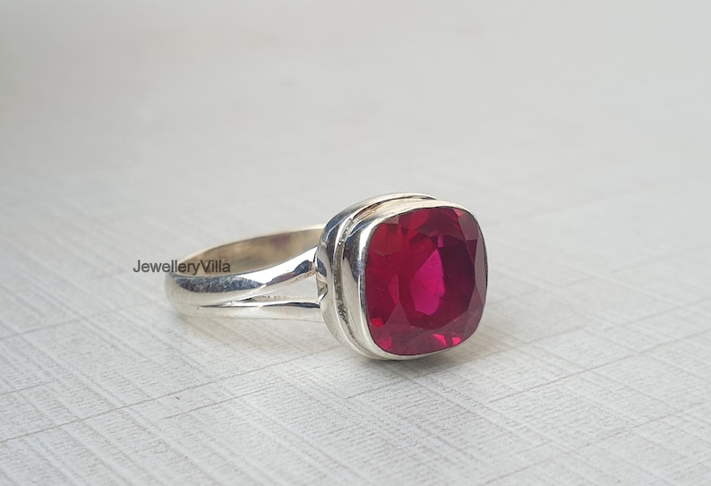 May include: A silver ring featuring a large, square-shaped, deep red gemstone.