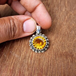 May include: A round pendant featuring a large, faceted, yellow gemstone set in a silver bezel. The pendant is surrounded by a silver halo of small beads.