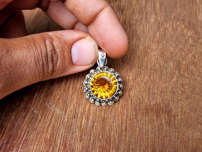 May include: A round pendant featuring a large, faceted, yellow gemstone set in a silver bezel. The pendant is surrounded by a silver halo of small beads.
