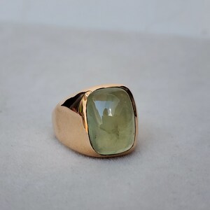Puede incluir: Un anillo de oro con una gran piedra preciosa verde claro engastada en una forma cuadrada.