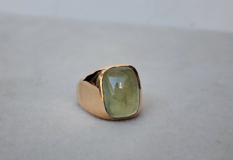 Puede incluir: Un anillo de oro con una gran piedra preciosa verde claro engastada en una forma cuadrada.