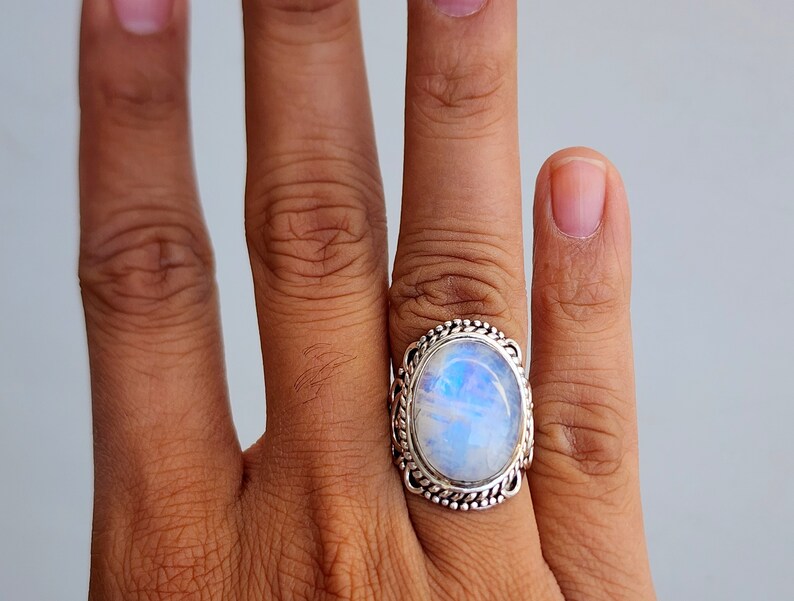 May include: A silver ring with a large oval moonstone set in a detailed silver band.