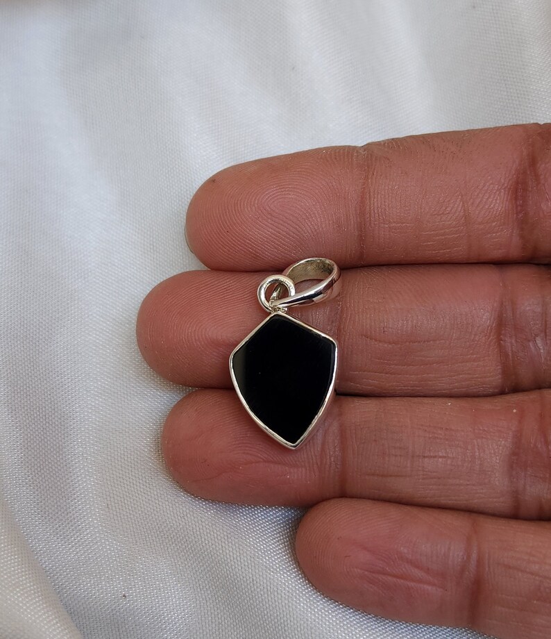 May include: A black onyx pendant in a silver shield shape with a silver bail.