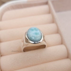 K&ouml;nnte beinhalten: Ein silberner Ring mit einem ovalen, hellblauen Edelstein. Der Ring befindet sich in einer Ringbox.