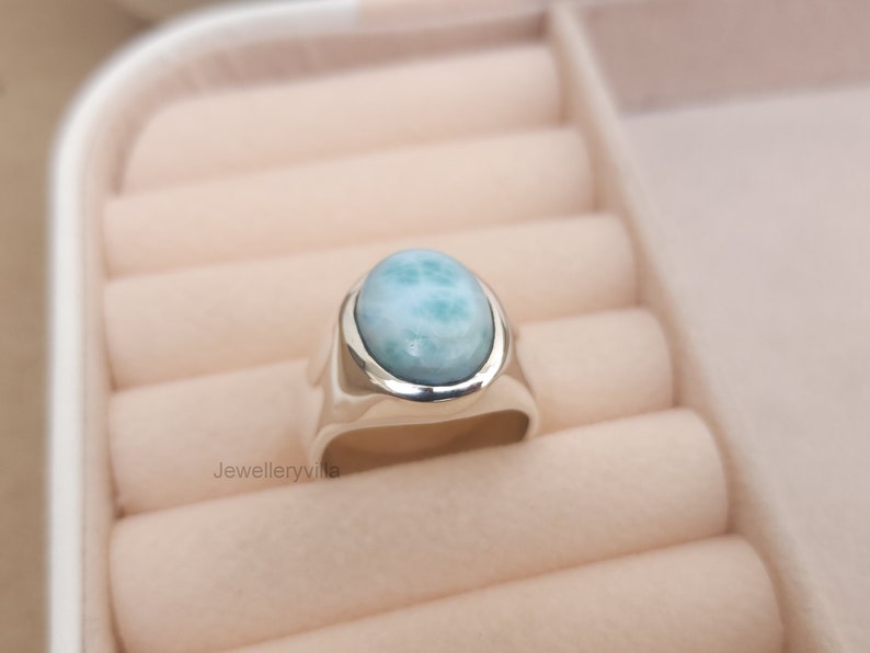 K&ouml;nnte beinhalten: Ein silberner Ring mit einem ovalen, hellblauen Edelstein. Der Ring befindet sich in einer Ringbox.
