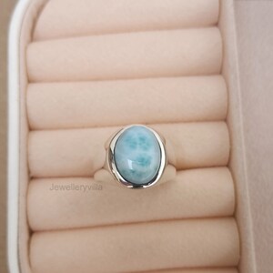 K&ouml;nnte beinhalten: Ein silberner Ring mit einem hellblauen ovalen Edelstein. Der Ring befindet sich in einer wei&szlig;en Ringbox.