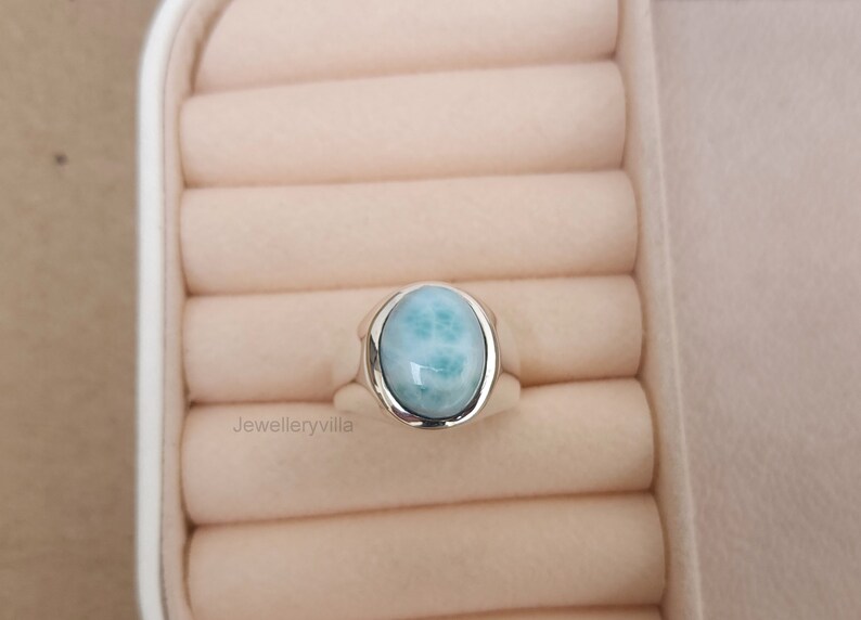 K&ouml;nnte beinhalten: Ein silberner Ring mit einem hellblauen ovalen Edelstein. Der Ring befindet sich in einer wei&szlig;en Ringbox.