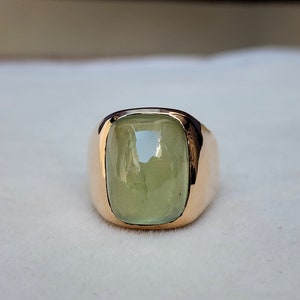 Puede incluir: Un anillo de oro con una gran piedra preciosa verde claro engastada en una forma cuadrada.