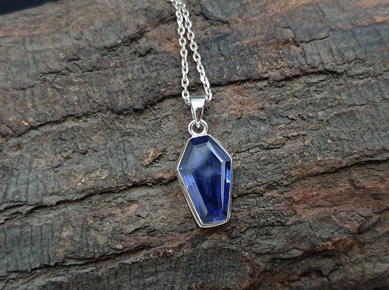 May include: A silver chain necklace with a blue gemstone pendant shaped like a coffin.