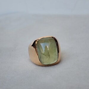Puede incluir: Un anillo de oro con una gran piedra preciosa verde claro engastada en un bisel cuadrado.