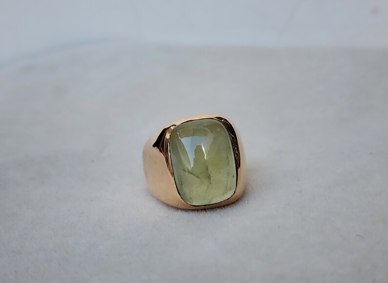 Puede incluir: Un anillo de oro con una gran piedra preciosa verde claro engastada en un bisel cuadrado.