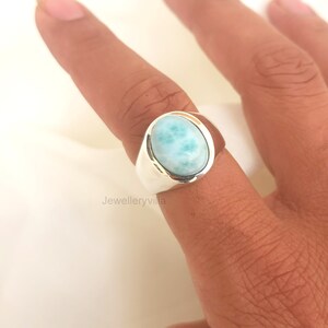 K&ouml;nnte beinhalten: Ein silberner Ring mit einem ovalen, hellblauen Edelstein. Der Edelstein hat ein marmoriertes Muster.