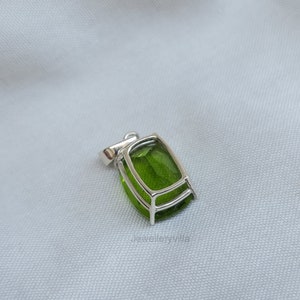 May include: A silver pendant with a large, green gemstone set in a bezel setting. The pendant has a simple design and is perfect for adding a touch of elegance to any outfit.