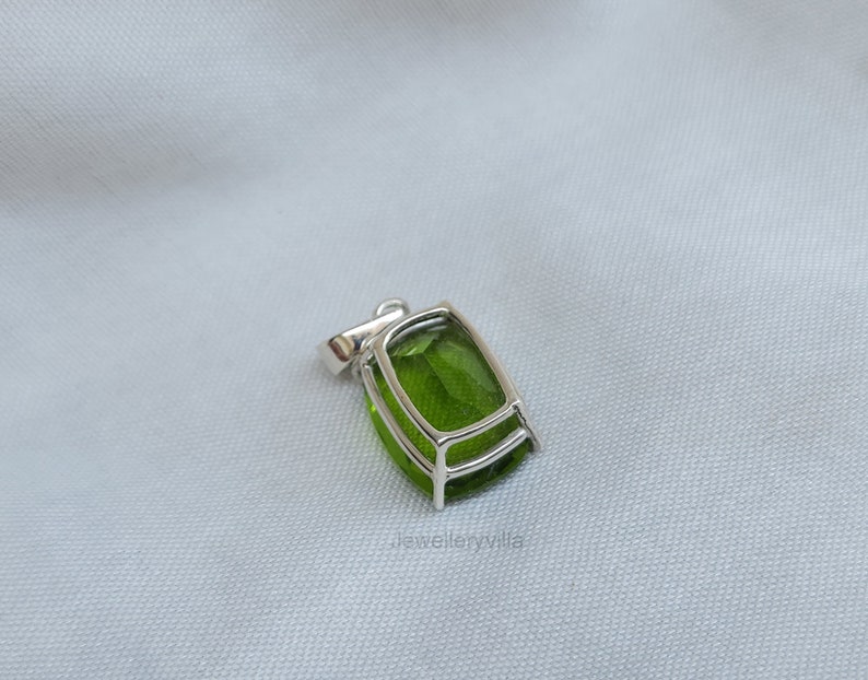 May include: A silver pendant with a large, green gemstone set in a bezel setting. The pendant has a simple design and is perfect for adding a touch of elegance to any outfit.