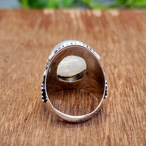 May include: Silver ring with a large oval-shaped white gemstone set in a detailed silver setting. The ring is shown from the back, revealing the smooth silver band.
