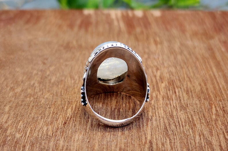 May include: Silver ring with a large oval-shaped white gemstone set in a detailed silver setting. The ring is shown from the back, revealing the smooth silver band.
