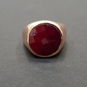 May include: A gold ring with a large, round, red gemstone.