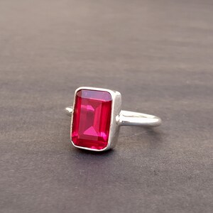 Op de afbeelding: Een zilveren ring met een grote, rechthoekige, felrode edelsteen.