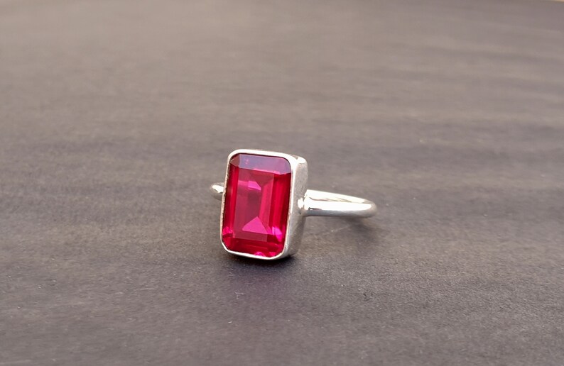 Op de afbeelding: Een zilveren ring met een grote, rechthoekige, felrode edelsteen.