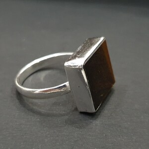 May include: A silver ring with a square-shaped brown gemstone.