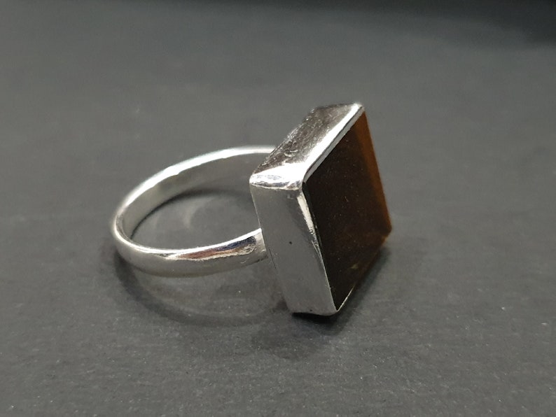 May include: A silver ring with a square-shaped brown gemstone.