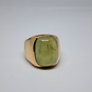 Puede incluir: Un anillo de oro con una gran piedra preciosa verde claro engastada en un engaste de bisel.