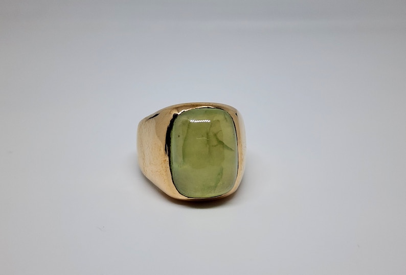 Puede incluir: Un anillo de oro con una gran piedra preciosa verde claro engastada en un engaste de bisel.