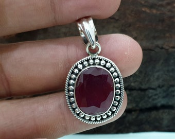 May include: A silver pendant with a red gemstone set in a beaded oval frame.