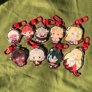 May include: A set of ten colorful character keychains with red metal rings. The characters are drawn in a cartoon style and feature a variety of expressions and poses.