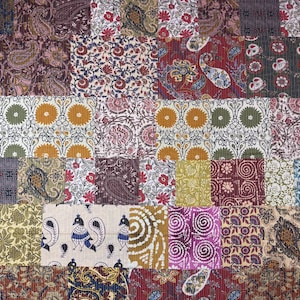 Può includere: Un tessuto patchwork con una miscela di quadrati di tessuto fantasia nei toni del rosso, viola, verde e oro. I motivi includono paisley, floreali e geometrici, creando una superficie vibrante e strutturata.