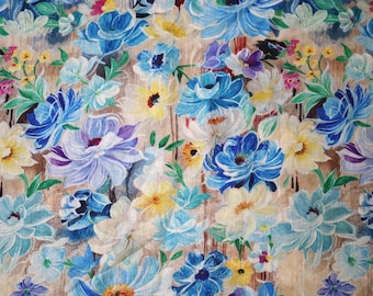May include: A floral pattern with large, stylised flowers in shades of blue, white, yellow, and purple. The flowers are set against a light brown background, creating a vibrant design. Suitable for fabric or wallpaper.