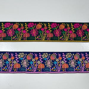 Könnte beinhalten: Zwei Streifen bestickte Stoffborte. Der obere Streifen ist dunkelgrün mit rosa, orangefarbenen und gelben Blumenmustern. Der untere Streifen ist dunkelblau mit hellblauen, rosa, orangefarbenen und weißen Blumenmustern. Beide zeigen feine Stickereien.