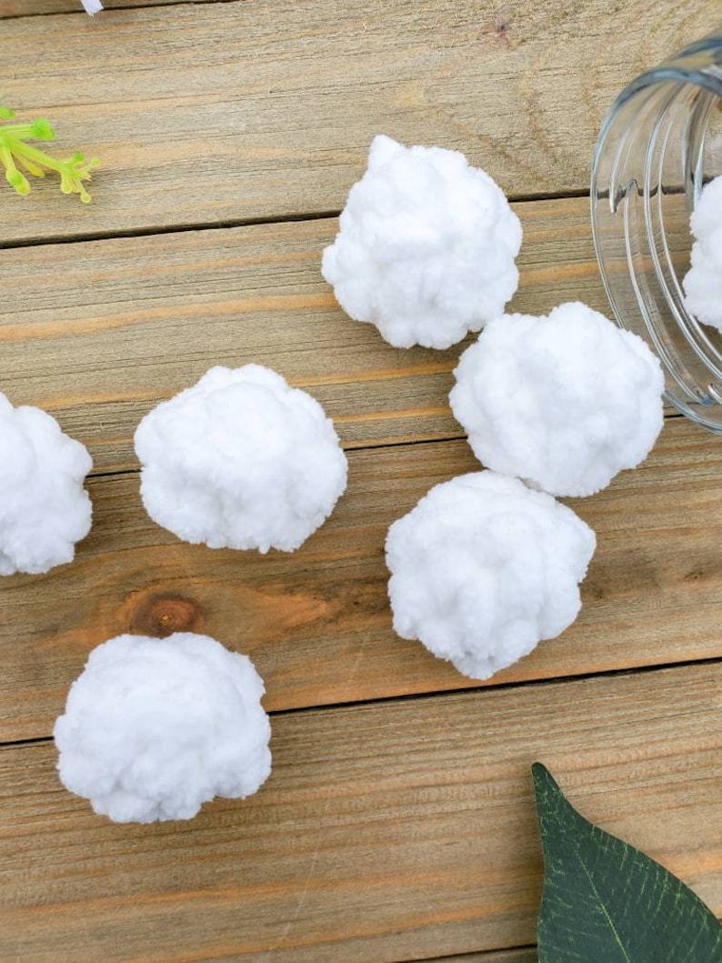 Op de afbeelding: Zes witte wattenbolletjes op een houten oppervlak. De wattenbolletjes zijn zacht en pluizig.