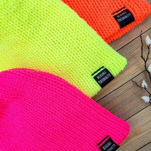 May include: Three knitted beanies in bright neon colors: pink, yellow, and orange. Each beanie has a black label sewn on the side that reads "Wearable Personality."